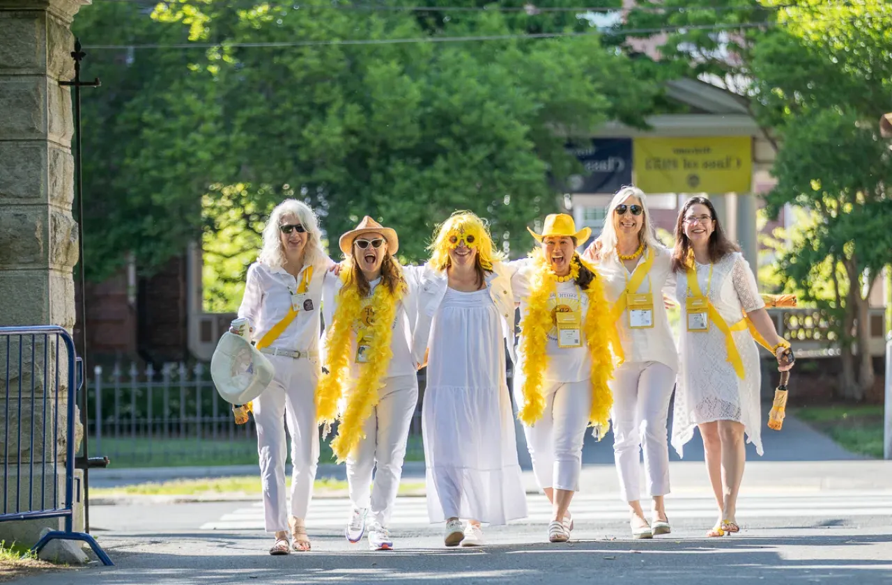 Several alums dressed in white arrive arm in arm on campus.