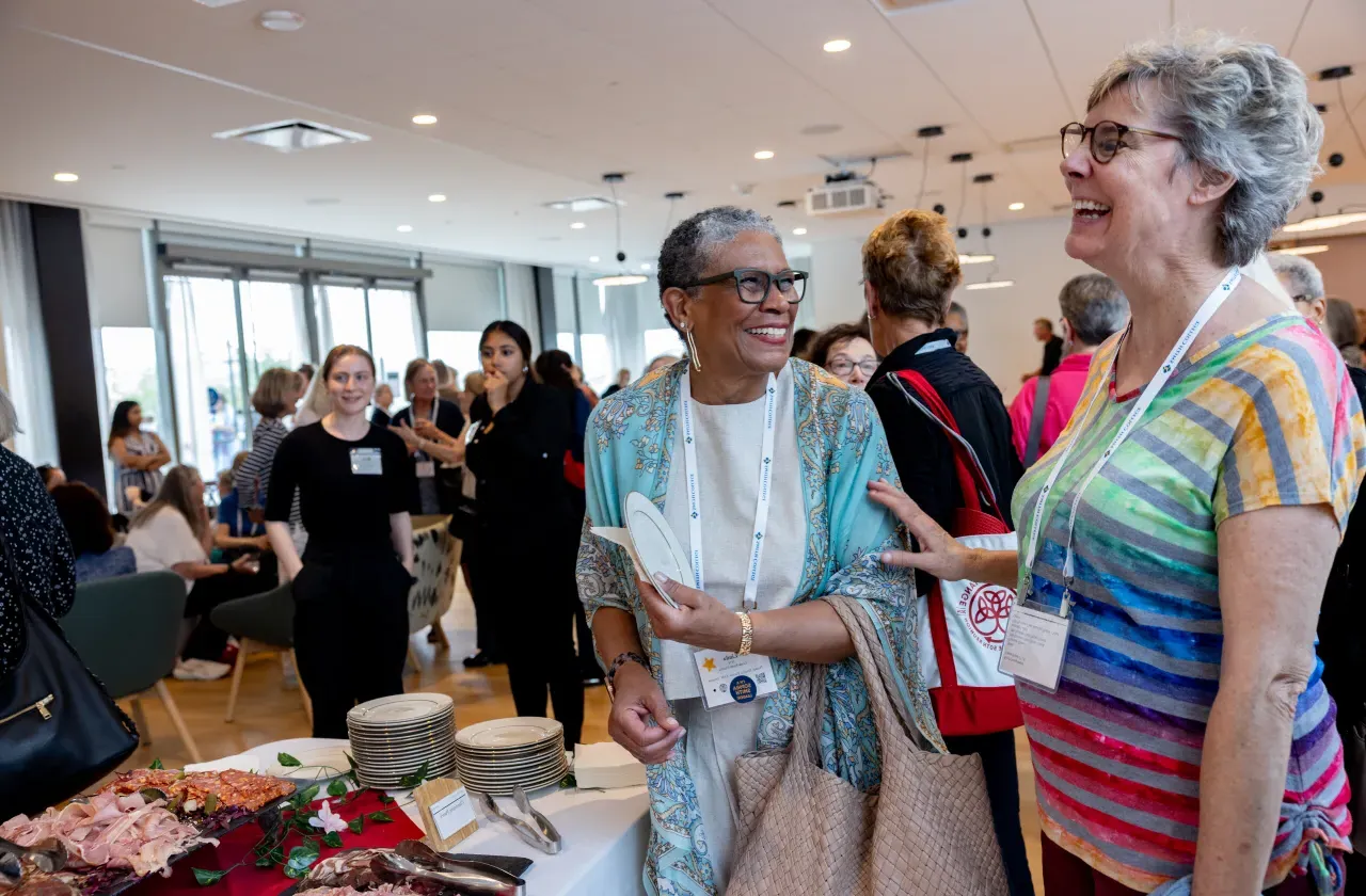 Two alums smiling and looking at each other while picking up plates, preparing to eat