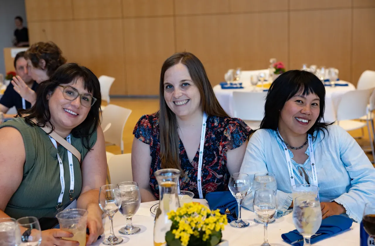 Three alums, seated together around a table, smile toward the camera