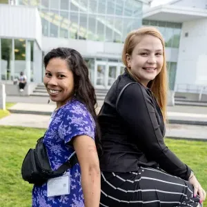 Two women smiling, standing back to back